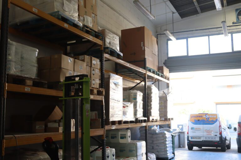 Interior de un almacén con una carretilla y la salida de este junto a una furgoneta de una tienda de piscinas