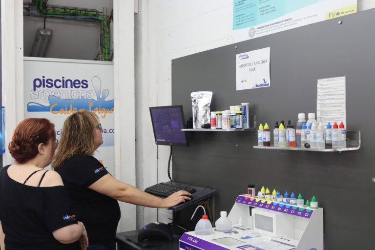 Dos empleadas mirando una pantalla de ordenador al lado de una maquina de análisis de agua de piscina